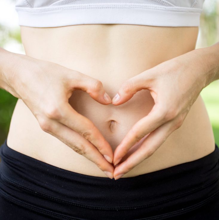 Close-up of female hands shaping heart on belly outdoors. Fitness and dieting concept
